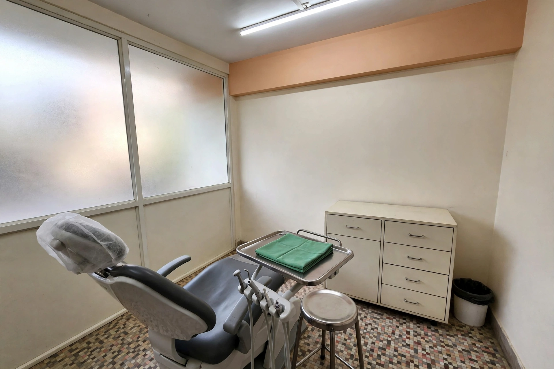 An empty treatment room with the dental chair ready and a folded green cloth on the tray